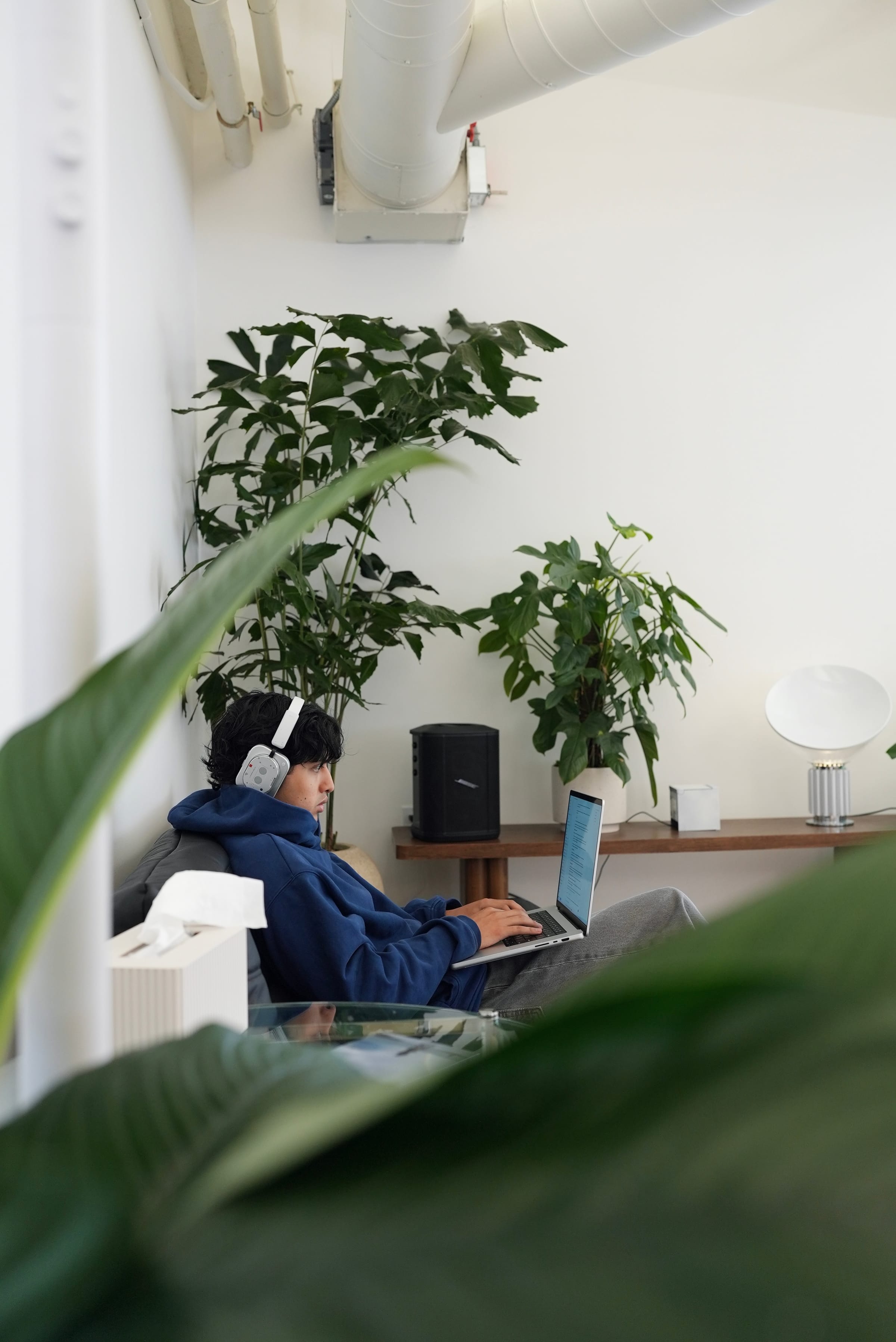 A Gumlooper working from the office couch in headphones, framed by plants